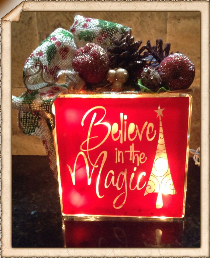 a lighted sign that says believe in the magic with christmas decorations and pine cones around it