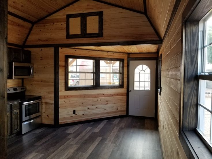 the interior of a tiny cabin with wood floors and walls, windows, and a stove top oven