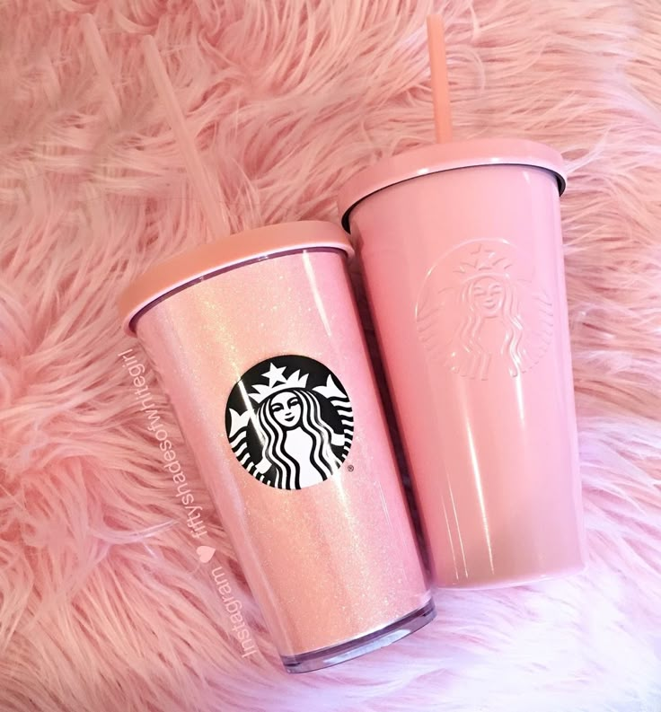 two pink starbucks cups sitting next to each other on top of a fur covered floor