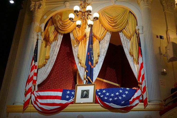 an american flag hanging in front of a window with gold drapes and draperies