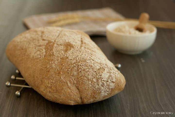 a loaf of bread sitting on top of a wooden table next to a bowl and spoon