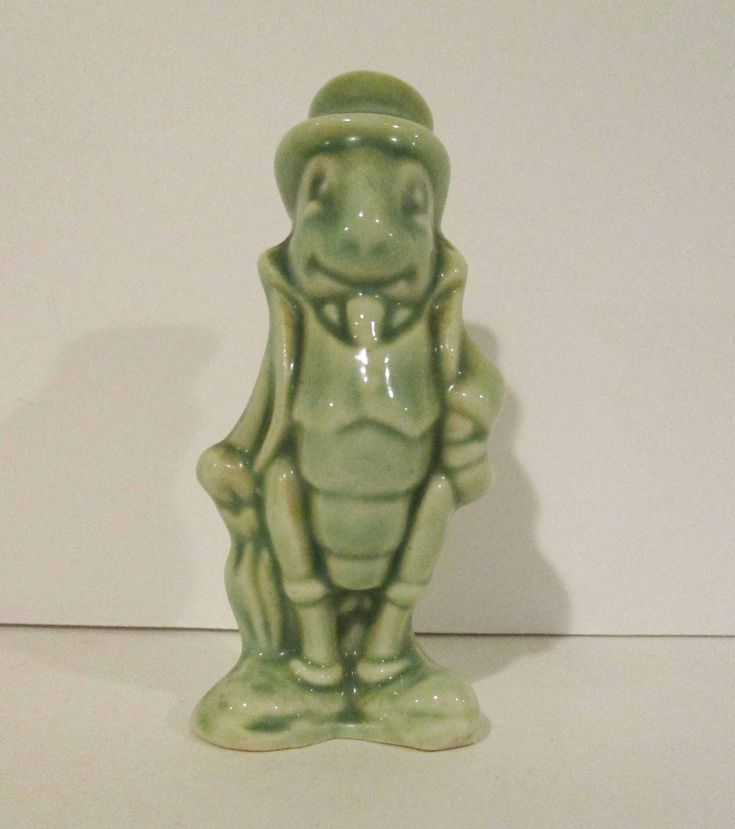 a green ceramic frog statue sitting on top of a white table next to a wall