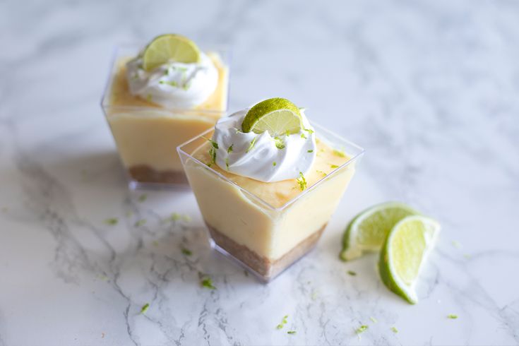 two desserts with lime and whipped cream in small cups on a marble countertop