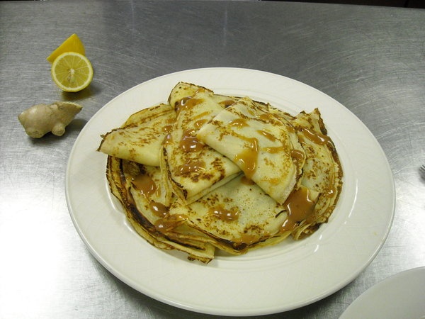 pancakes on a white plate with syrup drizzled over them and sliced lemons