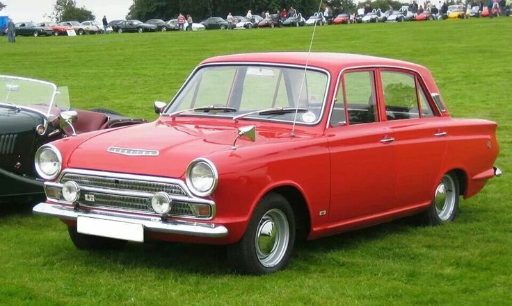 an old red car is parked in the grass next to other classic cars on display