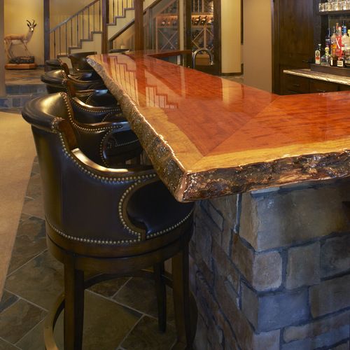 the bar is made out of wood and has black leather barstools in front of it