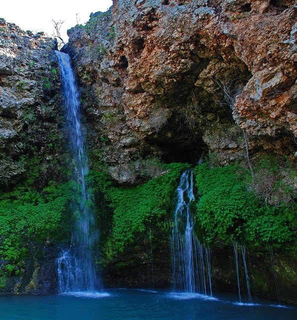 there is a small waterfall in the middle of some rocks and blue water below it