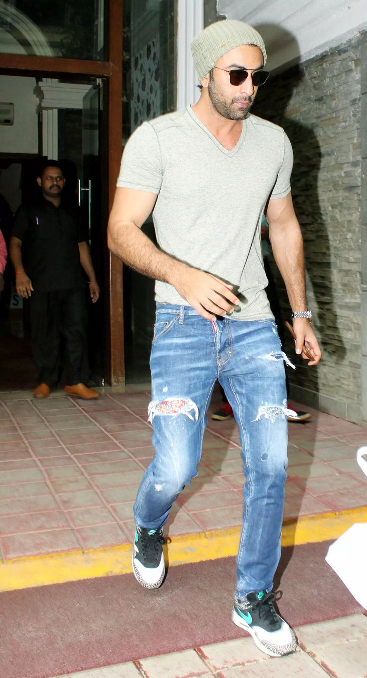 a man wearing ripped jeans and a beanie is seen leaving the building with his hands in his pockets