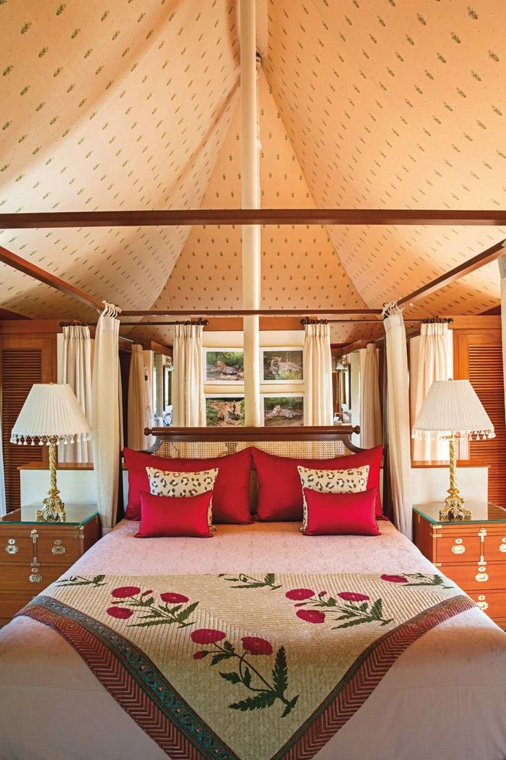 a bed with red pillows and two lamps on either side of the headboard in a bedroom