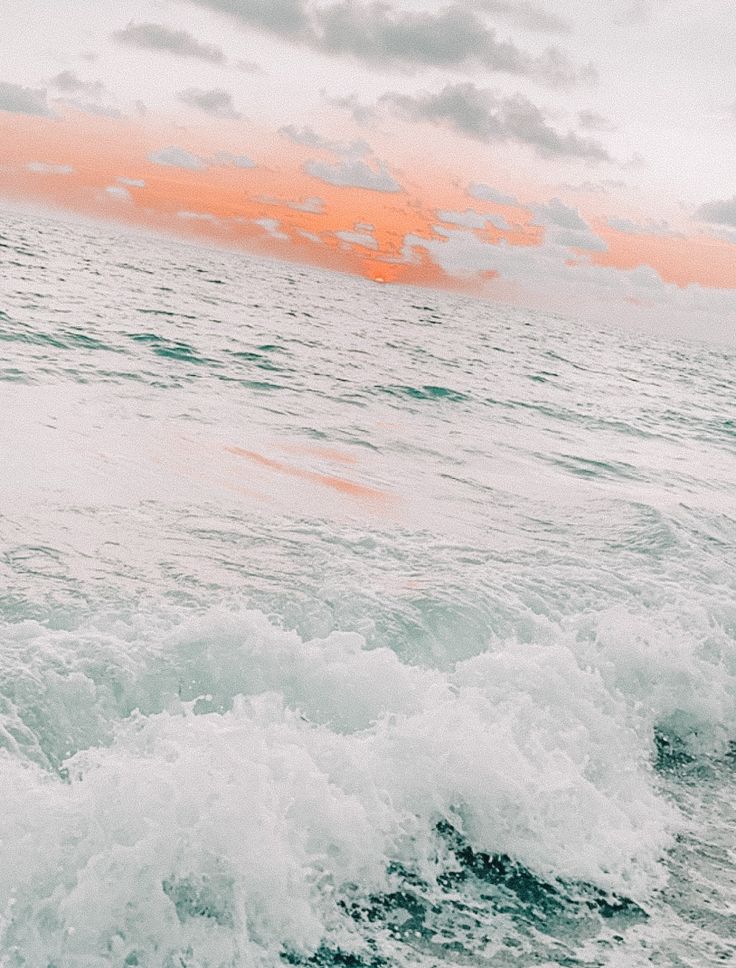 a man riding a surfboard on top of a wave in the ocean at sunset