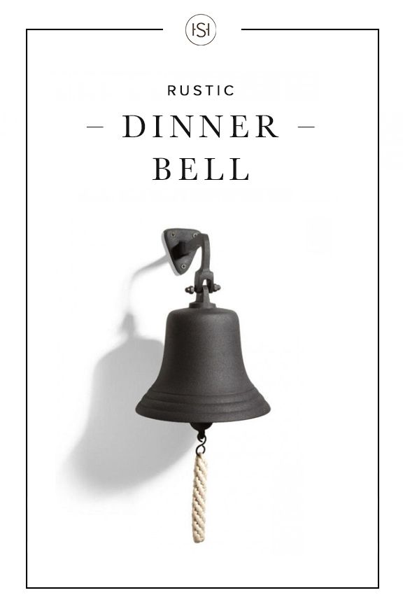 a black bell hanging from the side of a white wall with text reading rustic dinner bell