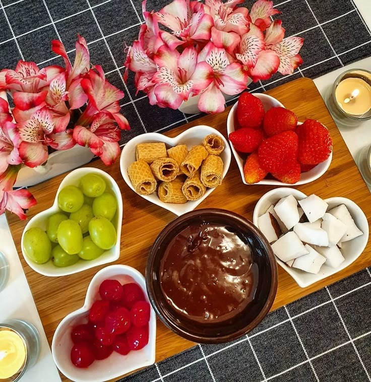 various fruits and dips are arranged in bowls on a cutting board next to flowers