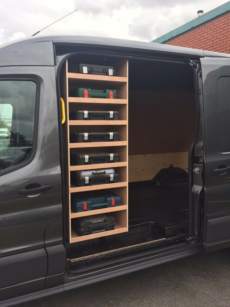 a van with its doors open is parked in front of a brick building and has several shelves on the side