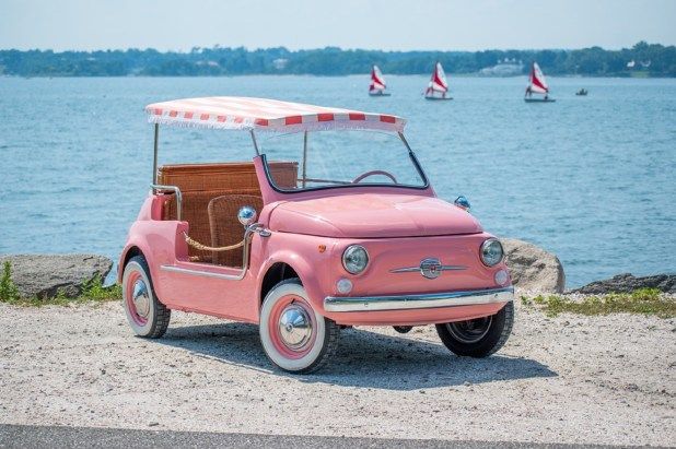 an old pink car parked by the water