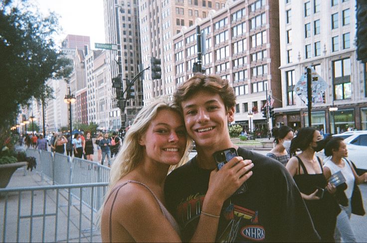 a man and woman standing next to each other in front of tall buildings on a city street