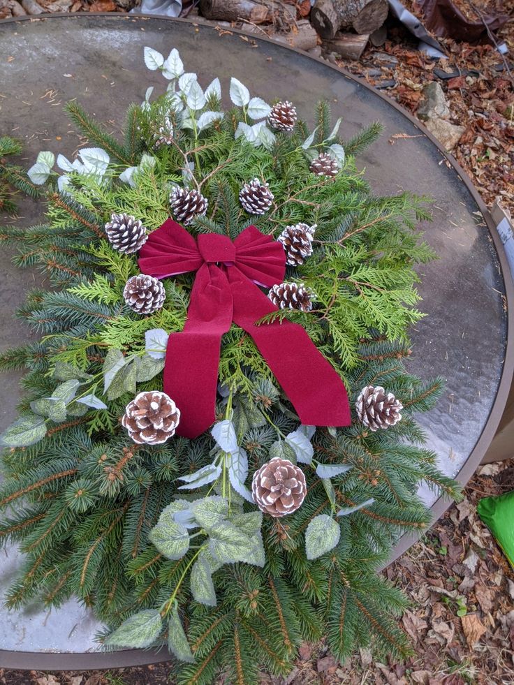 a christmas wreath with pine cones and evergreens on a metal platter in the woods