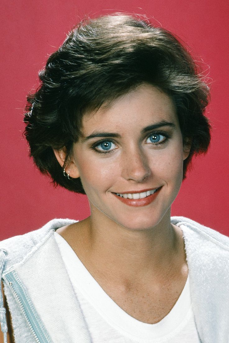 a woman with short hair and blue eyes posing for a photo in front of a red background