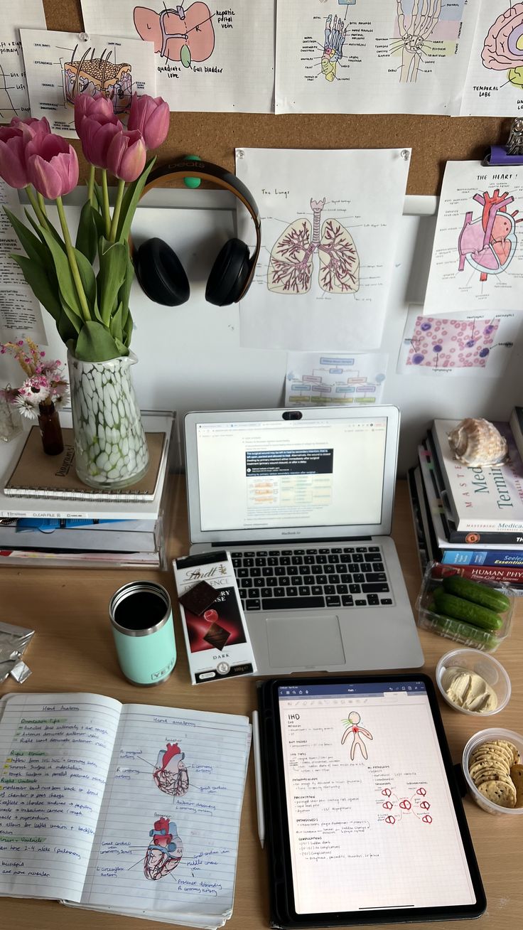 an open laptop computer sitting on top of a wooden desk next to books and flowers