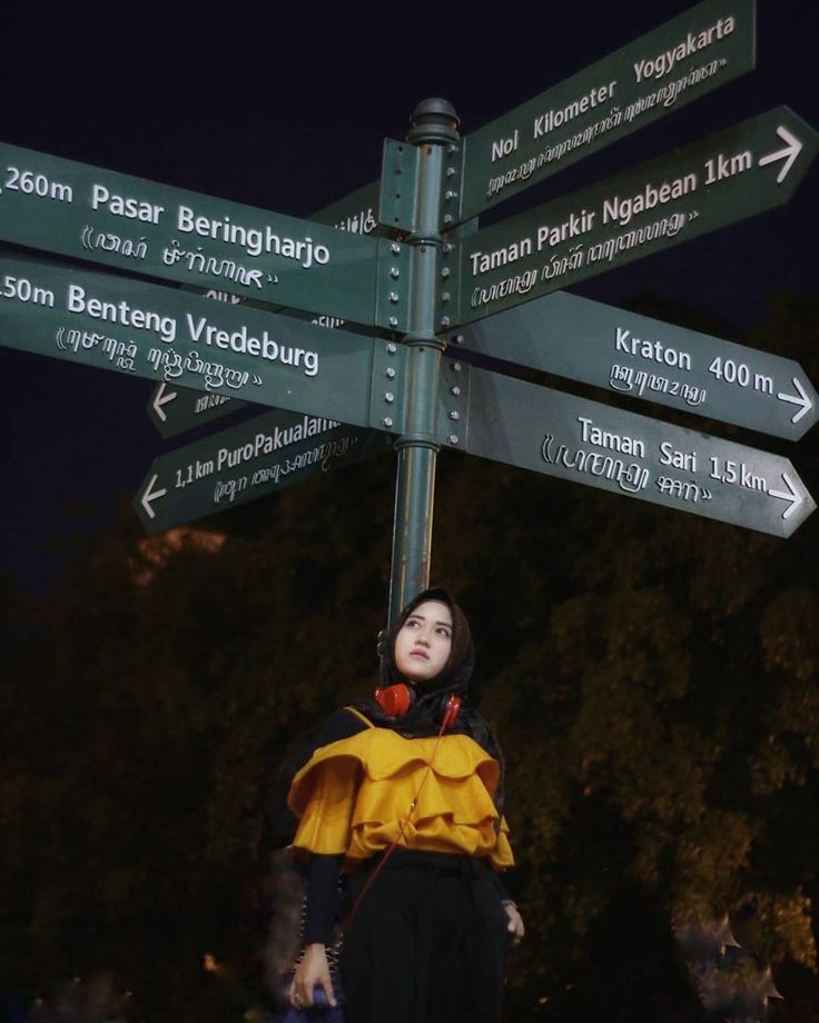 a woman standing next to a street sign with many signs pointing in the same direction