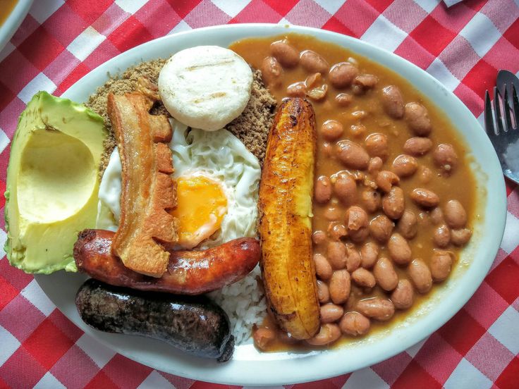 a white plate topped with beans, eggs and other foods on top of a red and white checkered table cloth