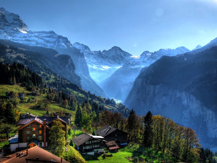 the mountains are covered in snow and green grass, while houses sit on top of them