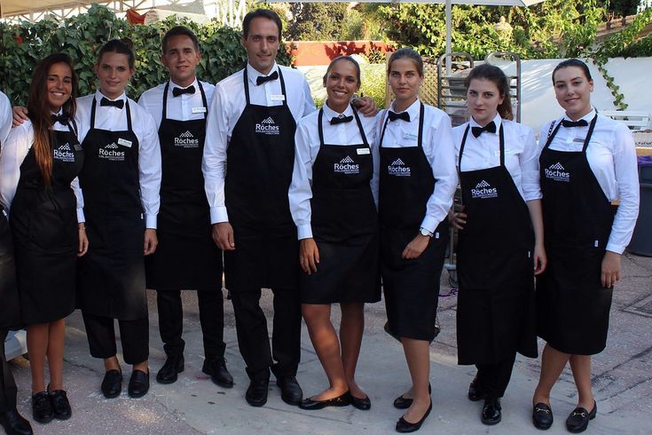 a group of people in black aprons and white shirts posing for a photo under an umbrella