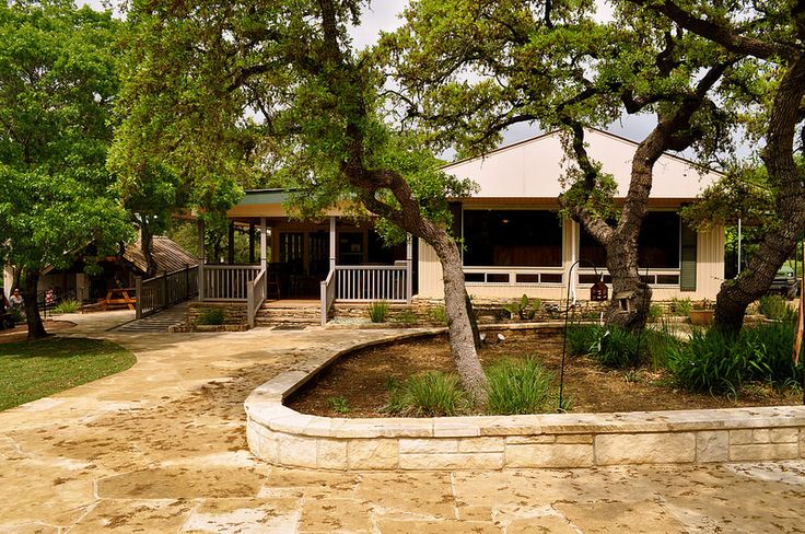 a house with trees in front of it on a dirt lot next to a fence