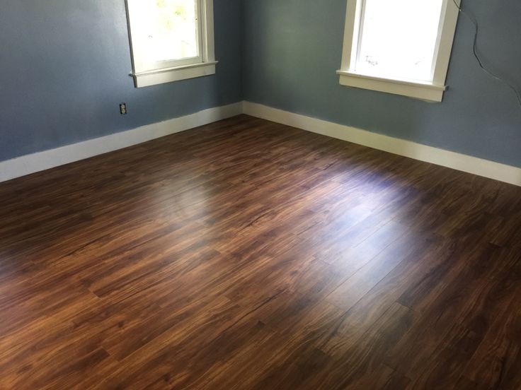 an empty room with hard wood flooring and two windows on the far wall is painted blue