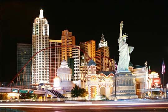 the statue of liberty is lit up at night in las vegas, nv with skyscrapers behind it