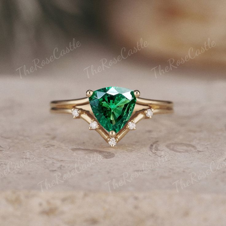 a green heart shaped diamond ring on top of a stone surface with diamonds around it