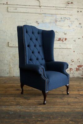 an upholstered blue wingback chair in front of a white brick wall and wooden floor