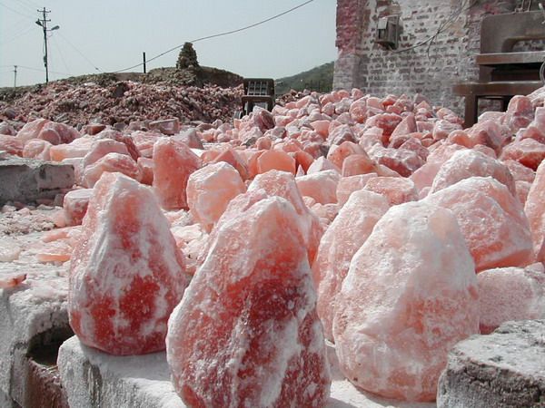 some very pretty pink rocks in front of a brick building with snow on them and one stone bench sitting next to it