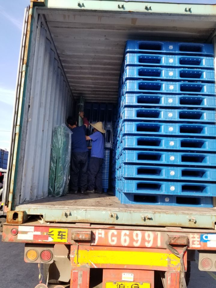 two men standing in the back of a truck with blue crates on it's flatbed