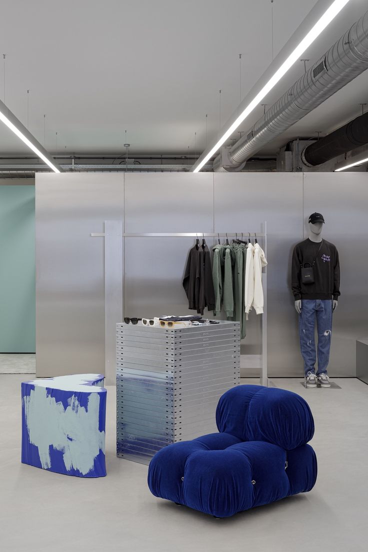 a man standing next to a blue chair in front of a display case with clothes on it