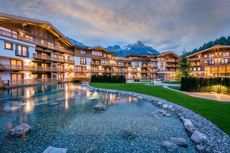 the building is lit up at night and reflecting in the water with mountains in the background