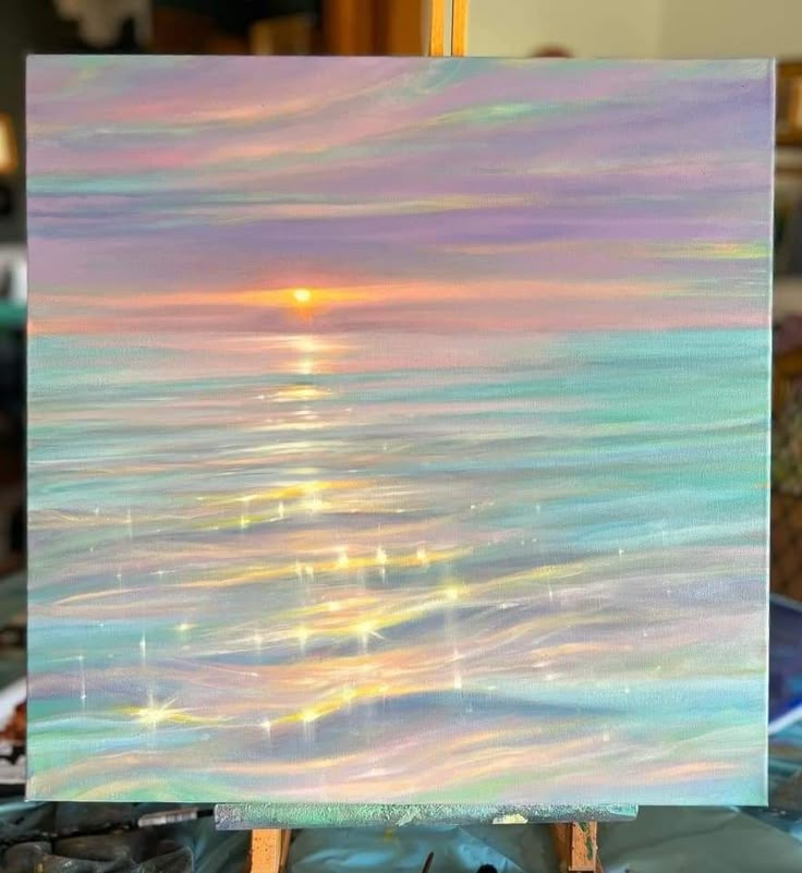 an easel with a painting on it and the sun in the sky above water