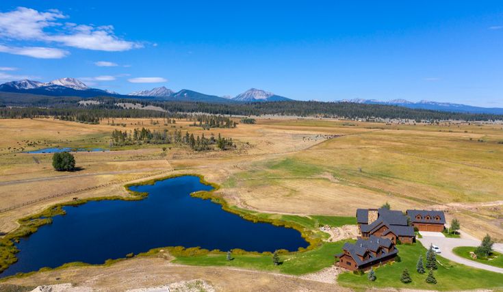 an aerial view of a home in the middle of a field with a lake and mountains behind it