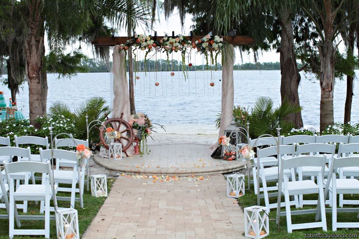 an outdoor ceremony set up with white chairs and flowers on the aisle, overlooking water