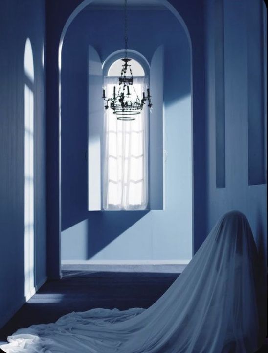 a bride's dress is draped in front of a window and chandelier