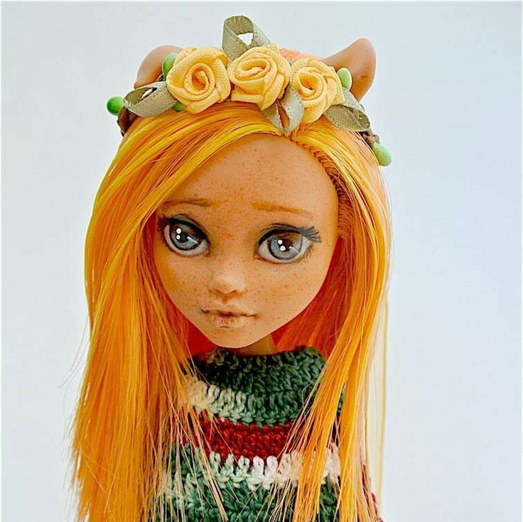 a doll with long orange hair wearing a knitted sweater and flower headpieces