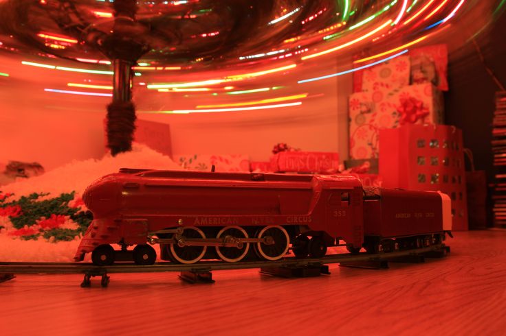 a toy train is on the tracks in front of a christmas tree with lights behind it