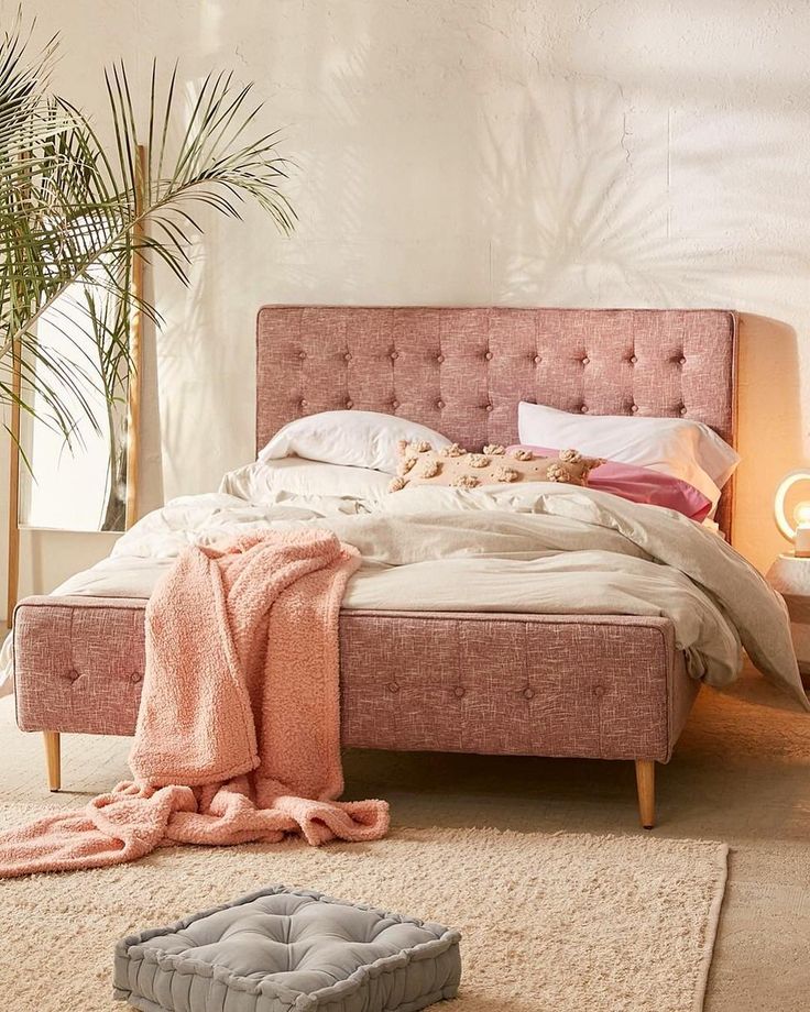 a bed with pink linens and pillows in a room next to a potted plant