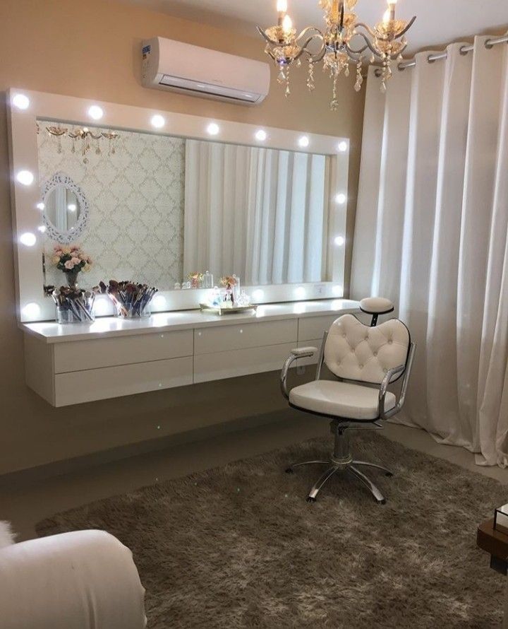 a white chair sitting in front of a mirror on top of a dresser under a chandelier