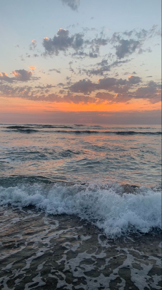 the sun is setting over the ocean with waves crashing on the shore and clouds in the sky