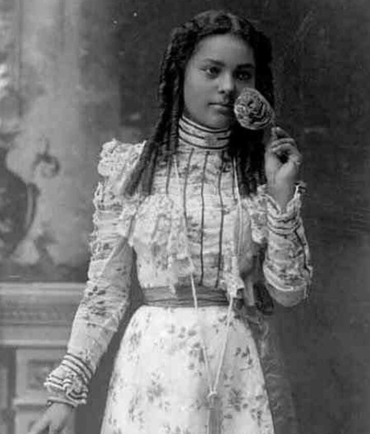 an old photo of a woman holding a flower in her right hand and looking at the camera