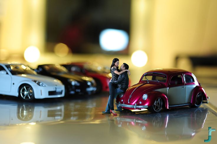 two miniature people standing next to some toy cars