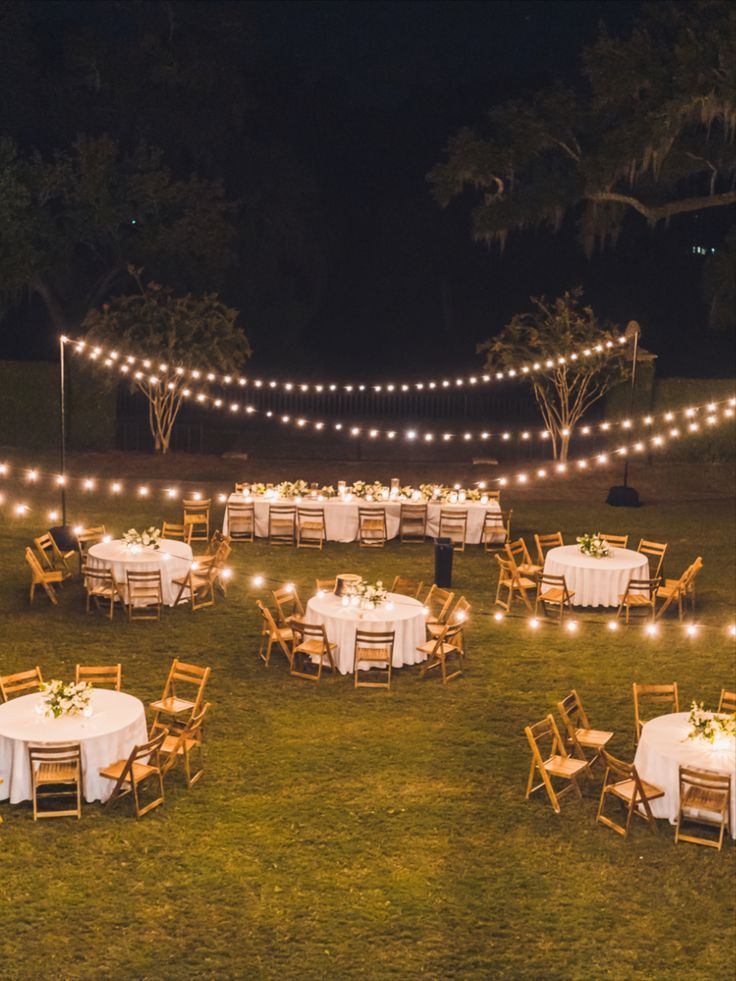 an outdoor dining area is lit up with string lights and white tablecloths set for dinner