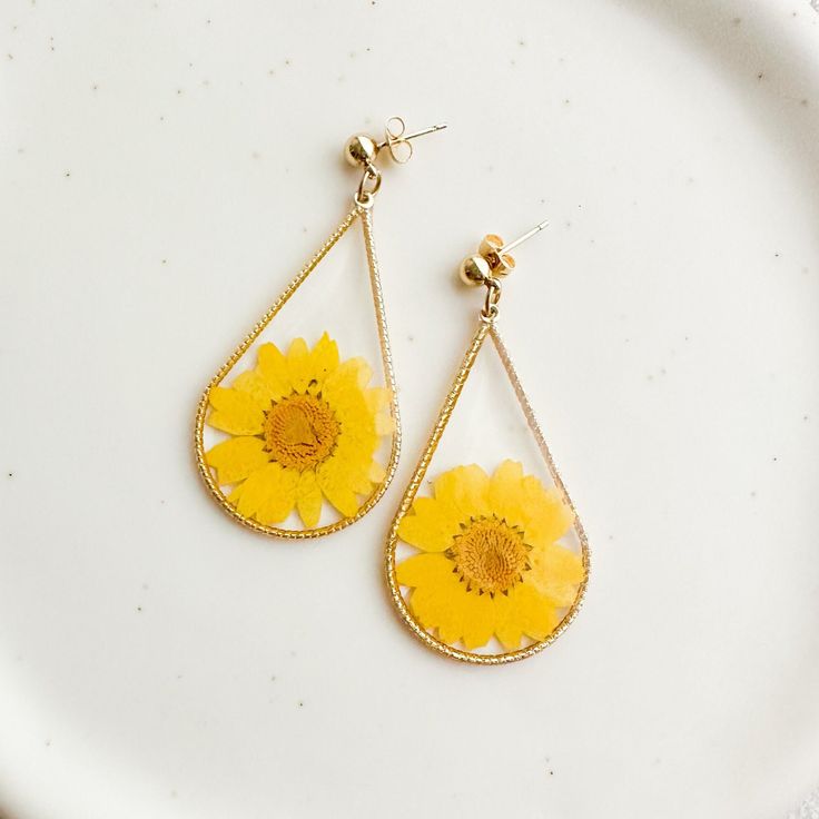 a pair of yellow dandelion earrings sitting on top of a white plate