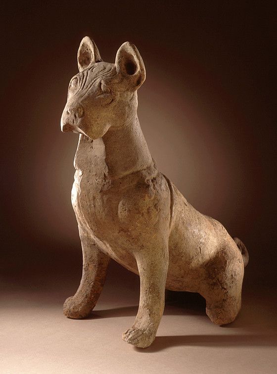 an old statue of a dog sitting on the ground with its head turned to the side