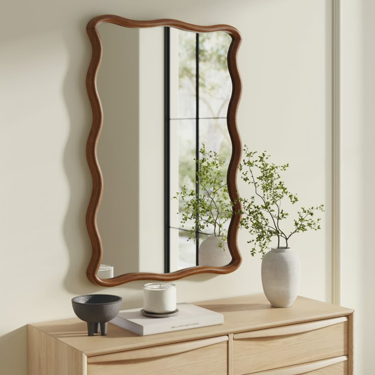 a mirror sitting on top of a wooden dresser next to a vase and potted plant